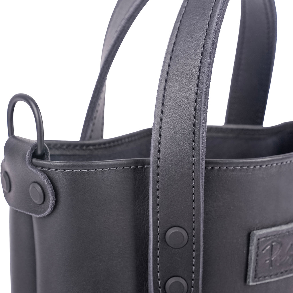 Close-up of a black leather small tote with visible stitching and Pask Fine Goods brand logo.